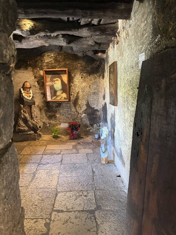 The stone corridor of the hermitage with a statue and portrait of Saint Charbel