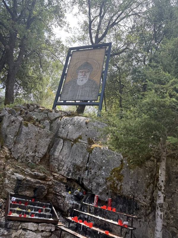 An icon of Saint Charbel above the rock, with red votive candles below