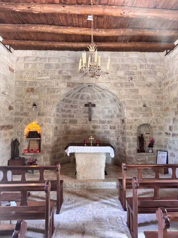 A small stone chapel with wooden pews and a simple altar